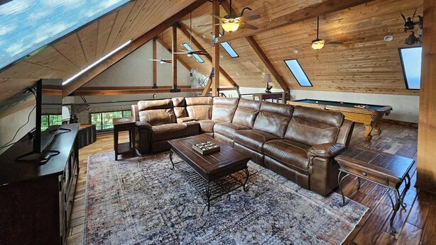 Ein geräumiger Loft mit hoher Decke, Holzbalken, einem großen Ledersofa und einem Billardtisch sowie Dachfenstern.