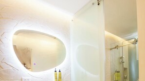Un baño moderno con tocador de madera, un espejo redondo y cabina de ducha de vidrio.