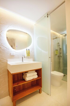 A modern bathroom with a wooden vanity, a round mirror, and a glass shower enclosure.