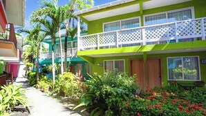 Un hotel de dos pisos con balcón, rodeado de exuberante follaje y palmeras.