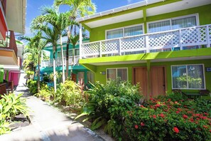 A two-story hotel with a balcony, surrounded by lush greenery and palm trees.