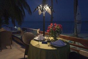 A table set for two with a 'Reserved' sign, a vase of red flowers, and a view of the ocean at night.