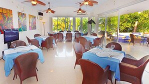 Un restaurante con mesas dispuestas para comer, ventiladores de techo y grandes ventanales que ofrecen vistas al exterior.