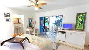 Habitación de hotel con cama, escritorio, televisión, balcón con vistas y ventilador de techo.