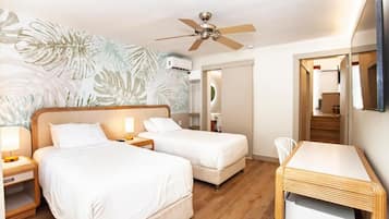 Quarto de hotel com duas camas, uma escrivaninha, um ventilador de teto e um espelho grande.