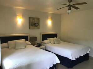 A hotel room with two single beds, a ceiling fan, bedside lamps, and a wall-mounted artwork.