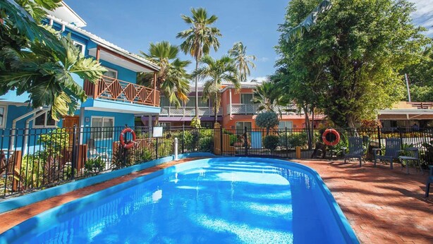 Una piscina rodeada de edificios con balcones, palmeras y un cielo despejado.