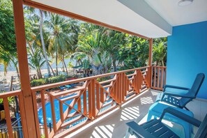 A balcony with a view of a pool and palm trees, a blue wall, and a chair.