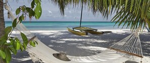 A hammock under a palm tree on a beach with a boat in the background. - Cocoplum Beach (San Andrés)