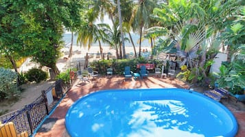 Uma piscina rodeada por palmeiras e cadeiras, com vista para a praia ao fundo.