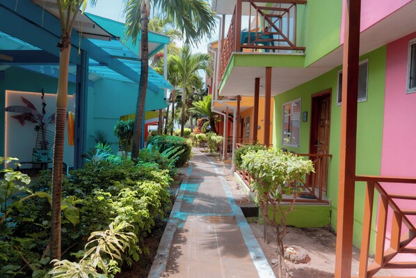 A pathway lined with greenery and buildings with balconies.
