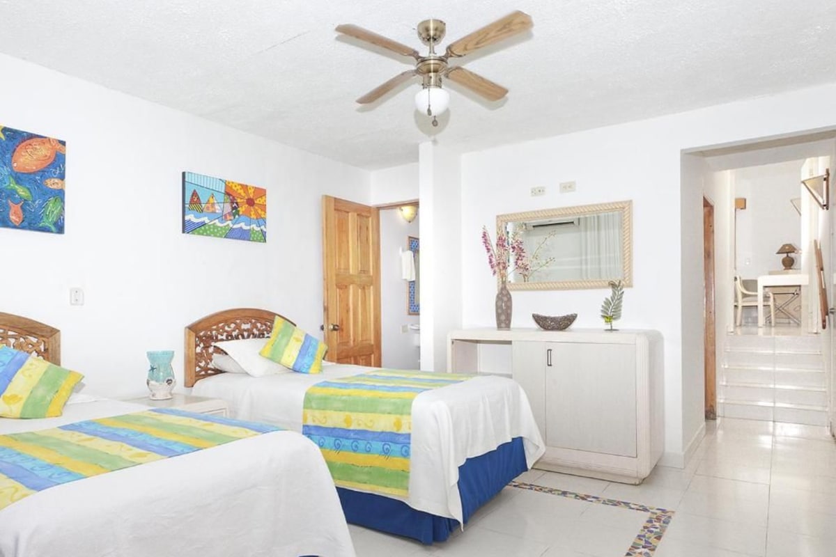 A hotel room with two beds, a ceiling fan, a white cabinet, and artwork on the walls.