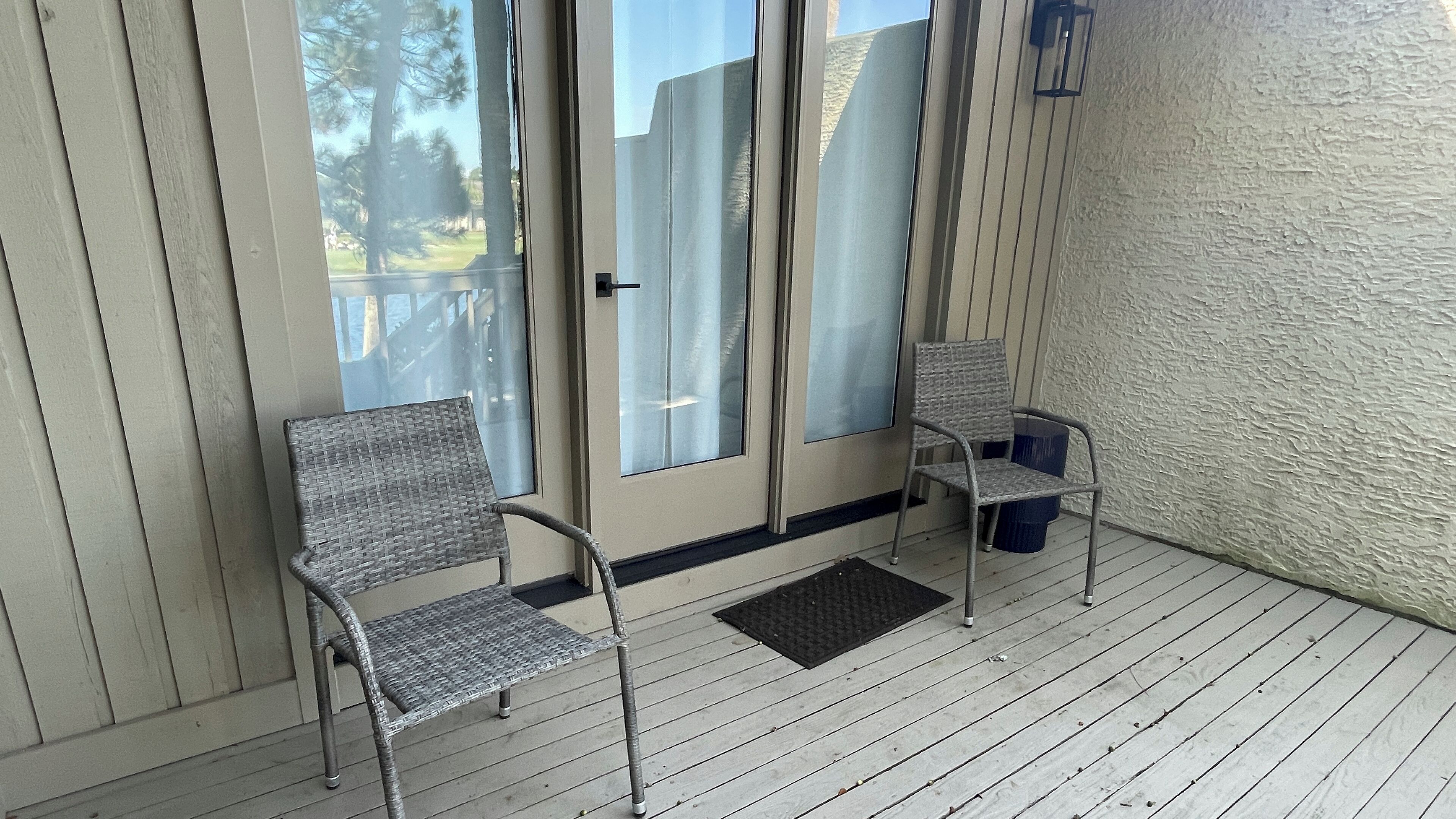 A covered porch with two wicker chairs and a small trash bin.