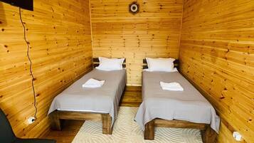 Une cabane avec deux lits en bois, une chaise noire, un luminaire en fibres tressées et une horloge murale.