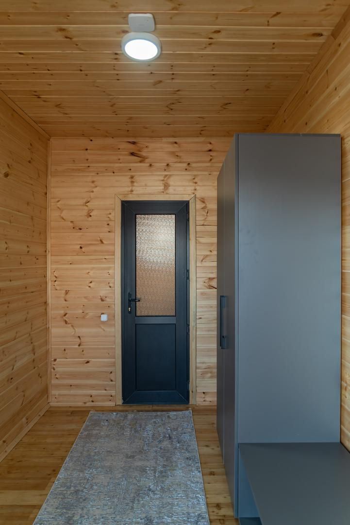 A wooden interior with a door, a refrigerator, and a ceiling light.