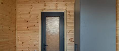 A wooden interior with a door, a refrigerator, and a ceiling light.