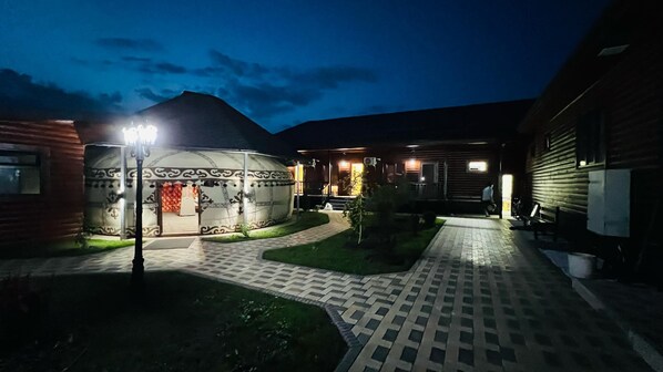 Un patio con una yurta tradicional, senderos pavimentados y un edificio con fachada de madera.