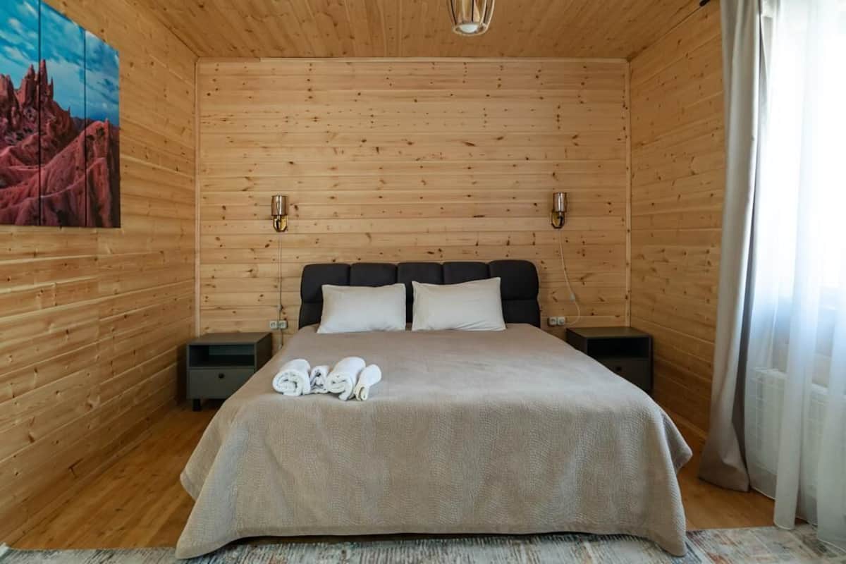 A wooden-paneled room with a bed, two bedside tables, and a painting on the wall.
