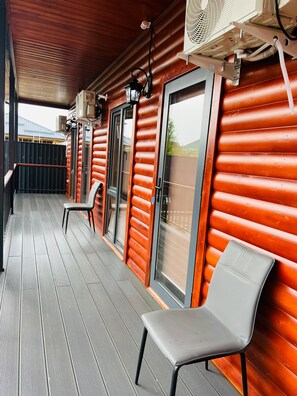 Una cabaña de madera con un porche cubierto, dos sillas y un ventanal con vistas.