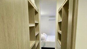 A narrow hallway leading to a bedroom with a bed and a small bedside table.