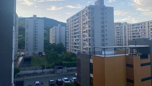 A view of high-rise residential buildings with balconies, a road with parked cars, and a green area in the foreground.