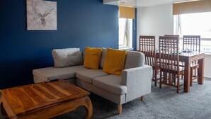 A living room with a grey sofa, wooden coffee table, and a dining table with chairs. - Modern Apartment with Dining, Workspace & Cooking (Motherwell, Glasgow)