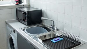 A compact kitchen with a washing machine, a microwave, and a sink with a drying rack. - Modern Apartment with Dining, Workspace & Cooking (Motherwell, Glasgow)