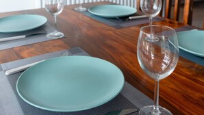 A dining table set with teal plates, cutlery, and wine glasses, with a wooden table and a chair in the background. - Modern Apartment with Dining, Workspace & Cooking (Motherwell, Glasgow)