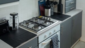 A kitchen with a gas stove, a coffee maker, and a toaster. There are cabinets, a countertop, and a window above the sink. - Modern Apartment with Dining, Workspace & Cooking (Motherwell, Glasgow)