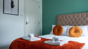 Habitación de hotel con cama, paredes blancas, una pared de acento color aguamarina y una puerta blanca.