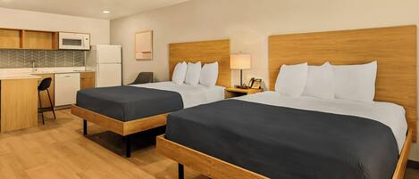 A hotel room with two beds, a kitchenette, and a desk.