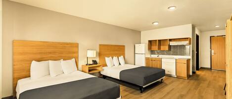 A hotel room with two beds, a kitchenette, and a separate bathroom.