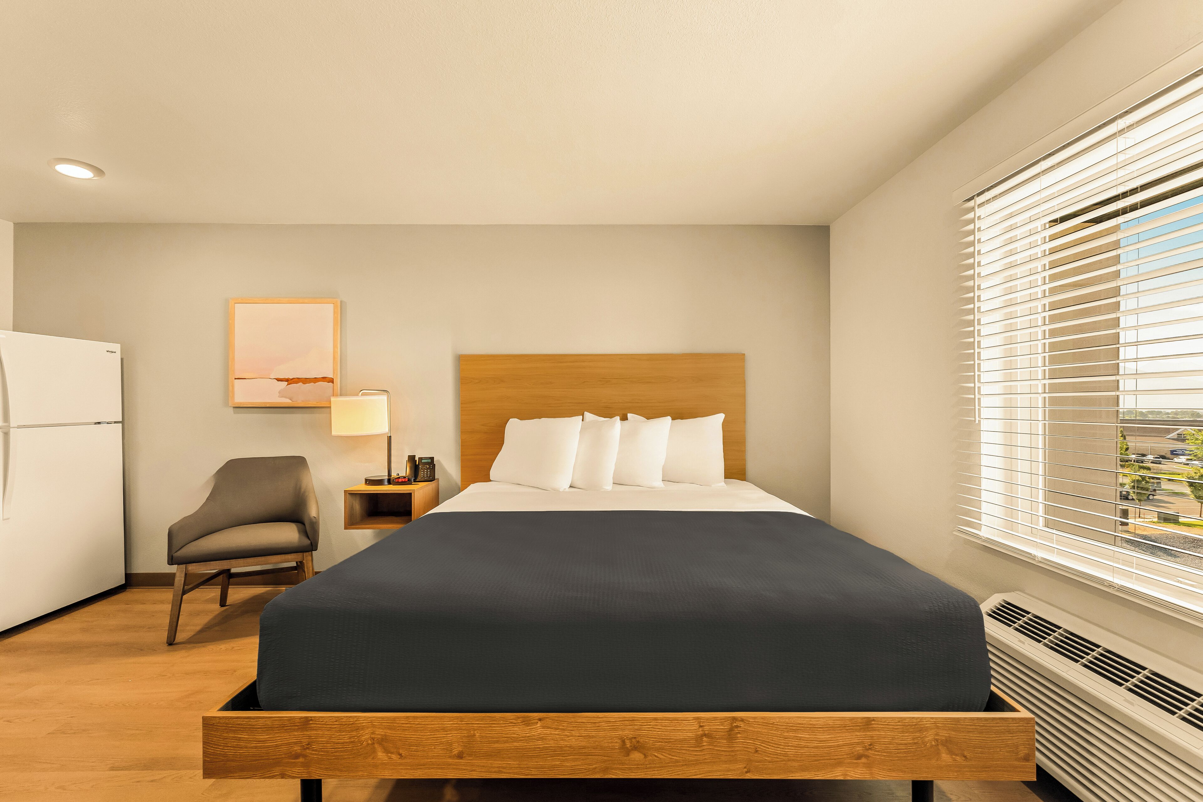 A hotel room with a bed, a chair, a desk with a lamp, and a window with blinds.