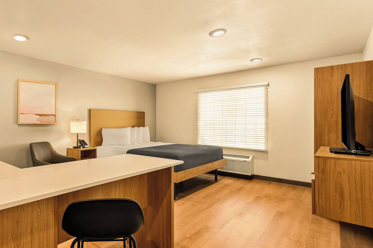 A hotel room with a bed, desk, chair, TV, and a window with blinds.