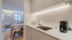A compact kitchen with a sink, a kettle, and a coffee maker. There is a dining area with a table and chairs.