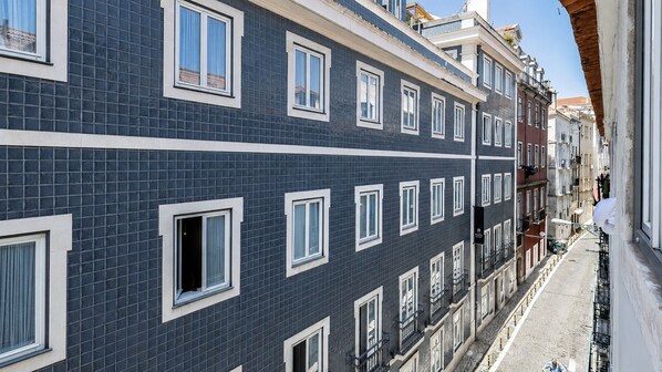 Un edificio de varios pisos con fachada oscura, numerosas ventanas y una calle estrecha.