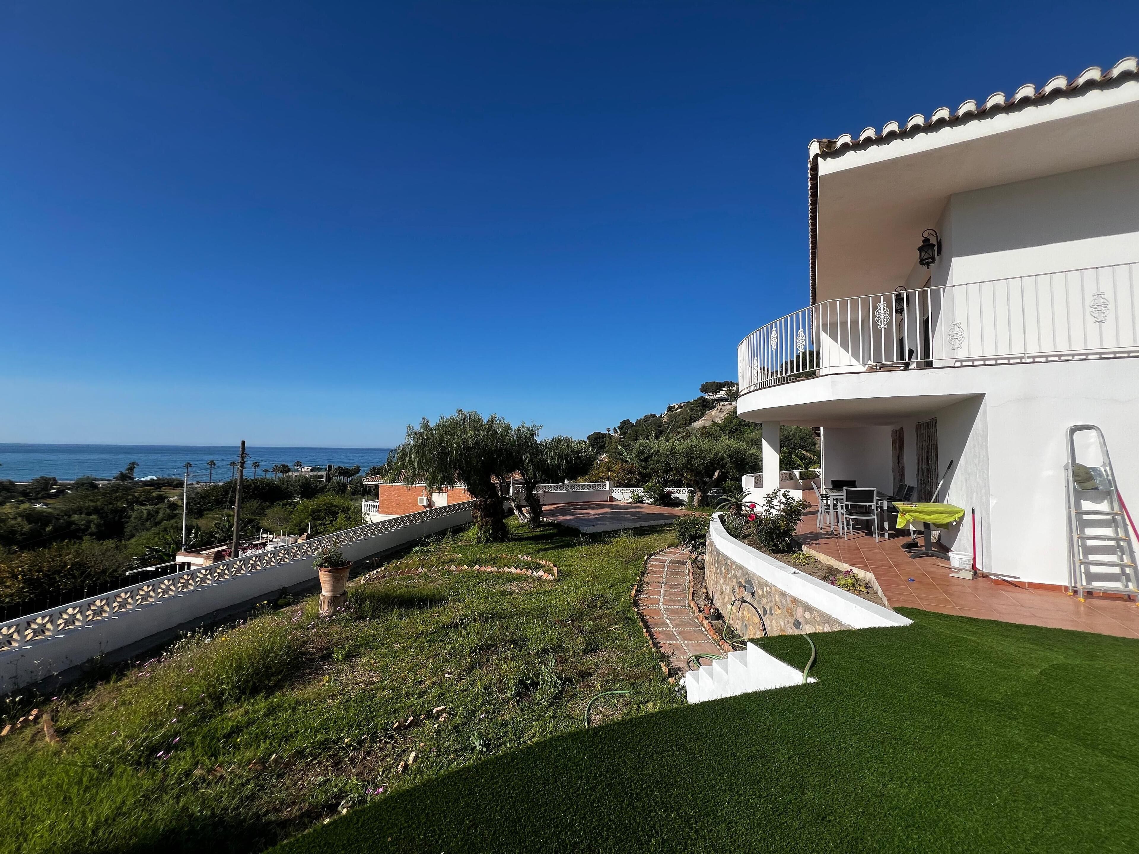 Un bâtiment blanc doté d’un balcon donnant sur un jardin aménagé et offrant une vue sur la mer.