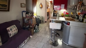A compact living space with a sofa, a dining area with a bar, and a kitchen area. - Cap d'agde - Appart 2 pers. Quiet ground floor with swimming pool - close to beach and shops (Agde)