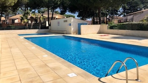 A swimming pool with tiled edges, surrounded by trees and buildings. - Cap d'agde - Appart 2 pers. Quiet ground floor with swimming pool - close to beach and shops (Agde)