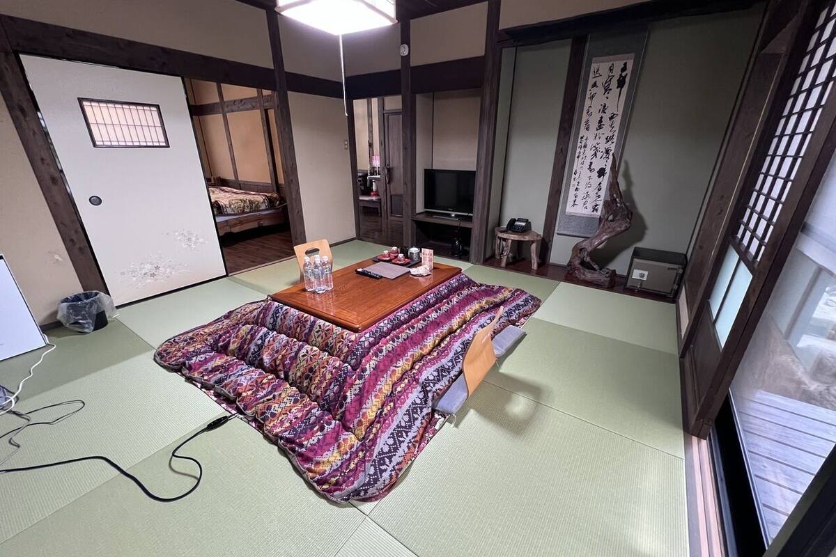 A tatami mat room with a low table, a television, and a traditional Japanese calligraphy scroll.
