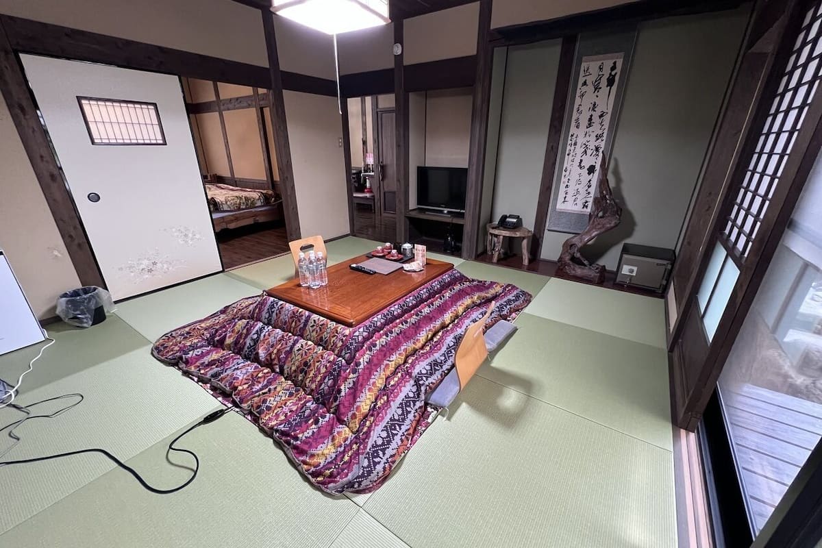Um espaço com esteiras de tatame, uma mesa baixa, uma televisão e um pergaminho de caligrafia japonesa tradicional.