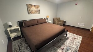 A bedroom with a bed, a nightstand, a chair, a lamp, and a painting on the wall.