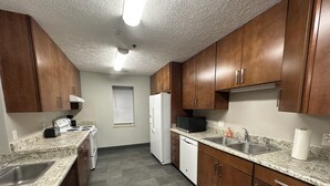 A kitchen with granite countertops, wooden cabinets, a white refrigerator, a microwave, and a double sink.