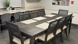 A dining area with a rectangular table, six chairs, and a kitchen counter in the background.