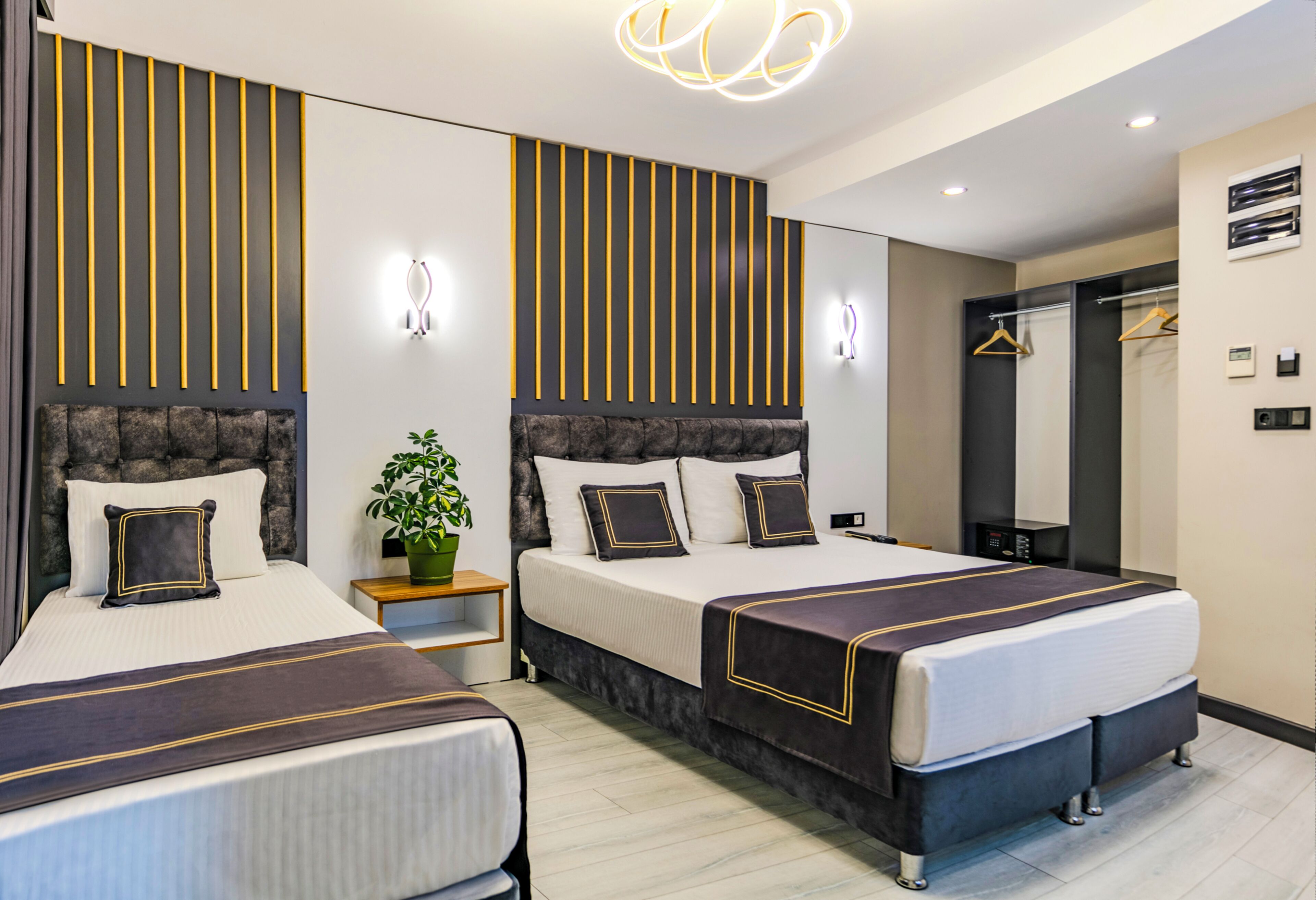 Ein Hotelzimmer mit zwei Betten, einer Zimmerpflanze, einem Spiegel und einer Pendelleuchte.