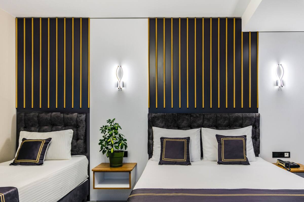 A hotel room with two beds, a potted plant, bedside tables, and wall-mounted light fixtures.