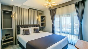 Habitación de hotel moderna con una cama grande, estanterías empotradas, una mesita de noche y vistas a la ciudad a través de amplias ventanas.
