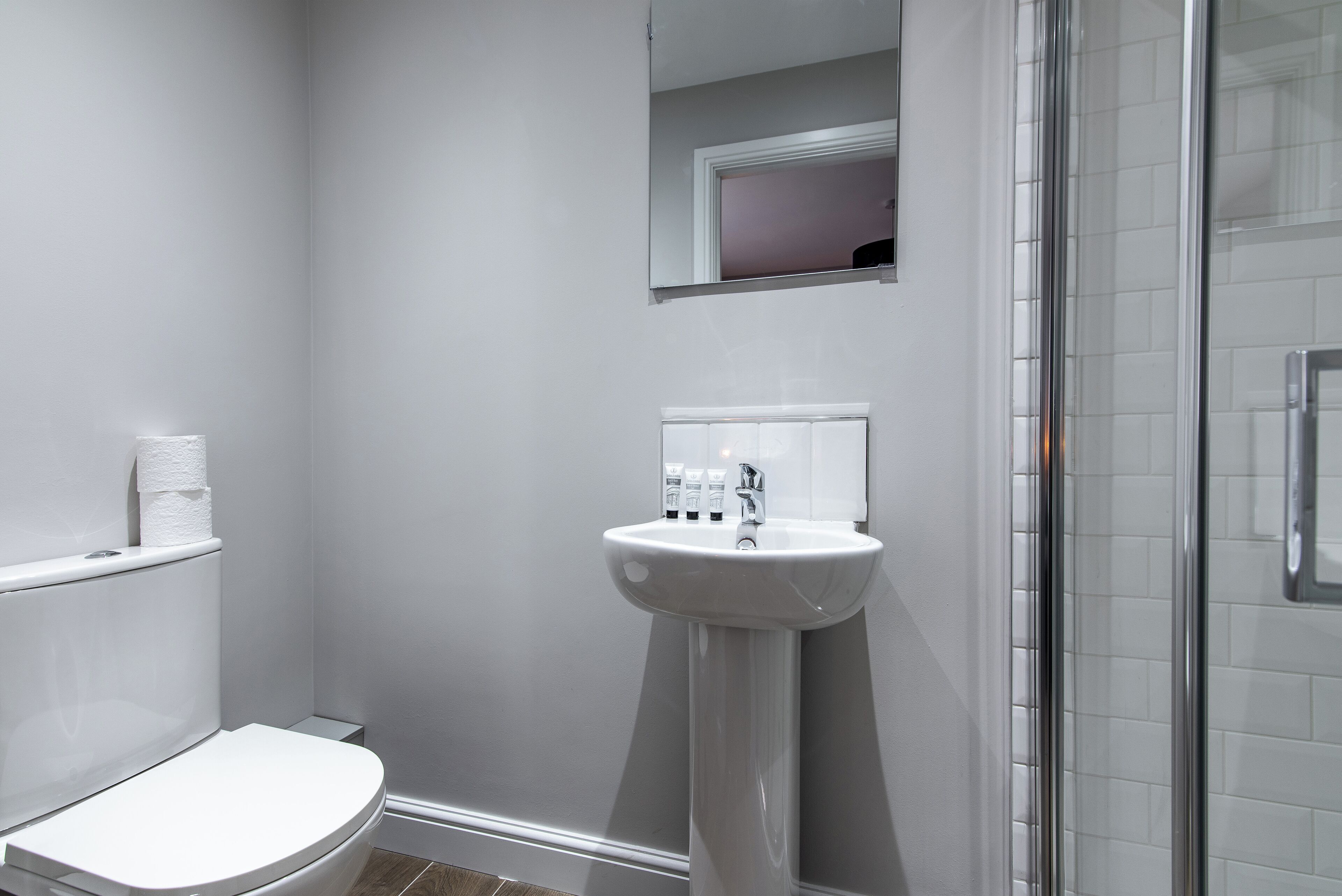 A bathroom with a white toilet, a pedestal sink, and a glass shower enclosure.