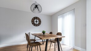 A dining area with a wooden table, six chairs, a black and white pendant light, and a wall clock. - Langdown House (Nottingham)