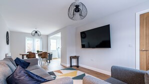 A modern living room with a grey sofa set, a flat-screen TV mounted on the wall, and a dining area in the background. - Langdown House (Nottingham)